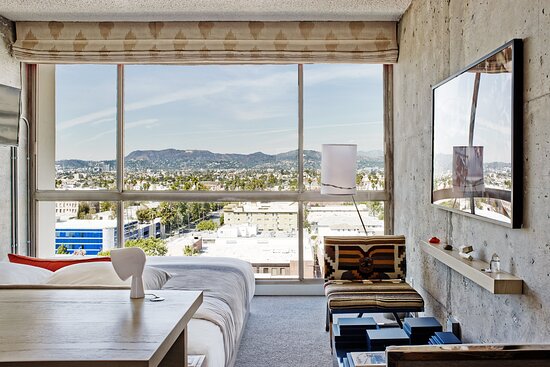 A hotel room with bare concrete walls and a glass wall looking over Los Angeles