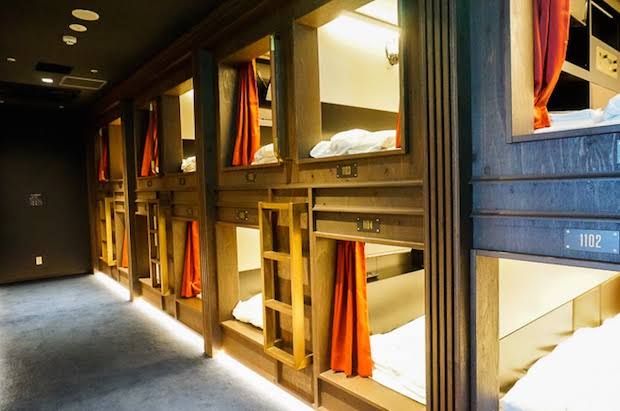 A corridor of stacked sleeping pods with lit openings and a step up to each berth