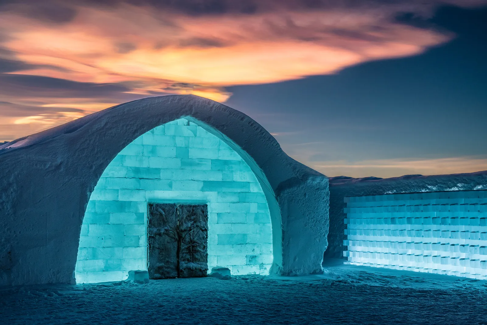 A carved ice room with a bed of ice, reindeer hides and blue light through the walls