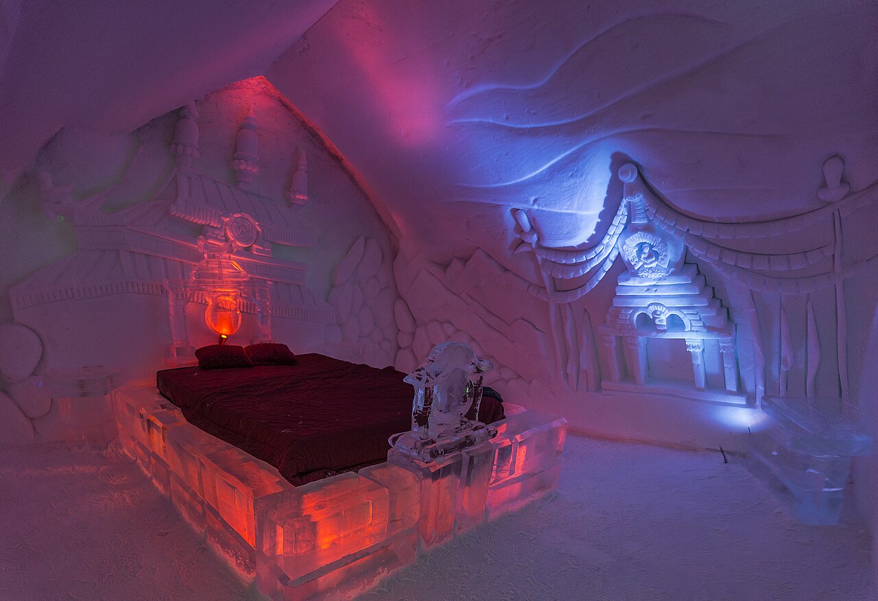 A vaulted corridor of snow with carved walls leading past doorways to ice rooms